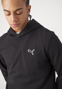 Felpa nera con cappuccio e tasca a marsupio, caratterizzata da un logo Puma ricamato bianco sul petto. Tessuto morbido e liscio con una vestibilità rilassata.