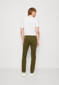 Olive green slim-fit pants with a smooth fabric finish, five pockets, and subtle stitching details, paired with a plain white T-shirt.