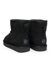 Par sort sorte ruskindsankelstøvler med flade gummisåler og trækketag, set bagfra på en hvid baggrund.