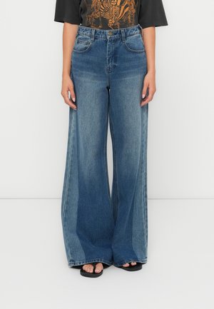 Lichtblauwe denim jeans met wijde pijpen en een hoge taille, voorzien van twee voorkruiden en een gladde textuur, gecombineerd met zwarte flip-flops.