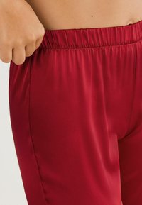 Rode joggers van satijnachtige stof met een elastische tailleband, met een gladde textuur en een aangesloten silhouet. Geen zichtbare patronen of hardware.