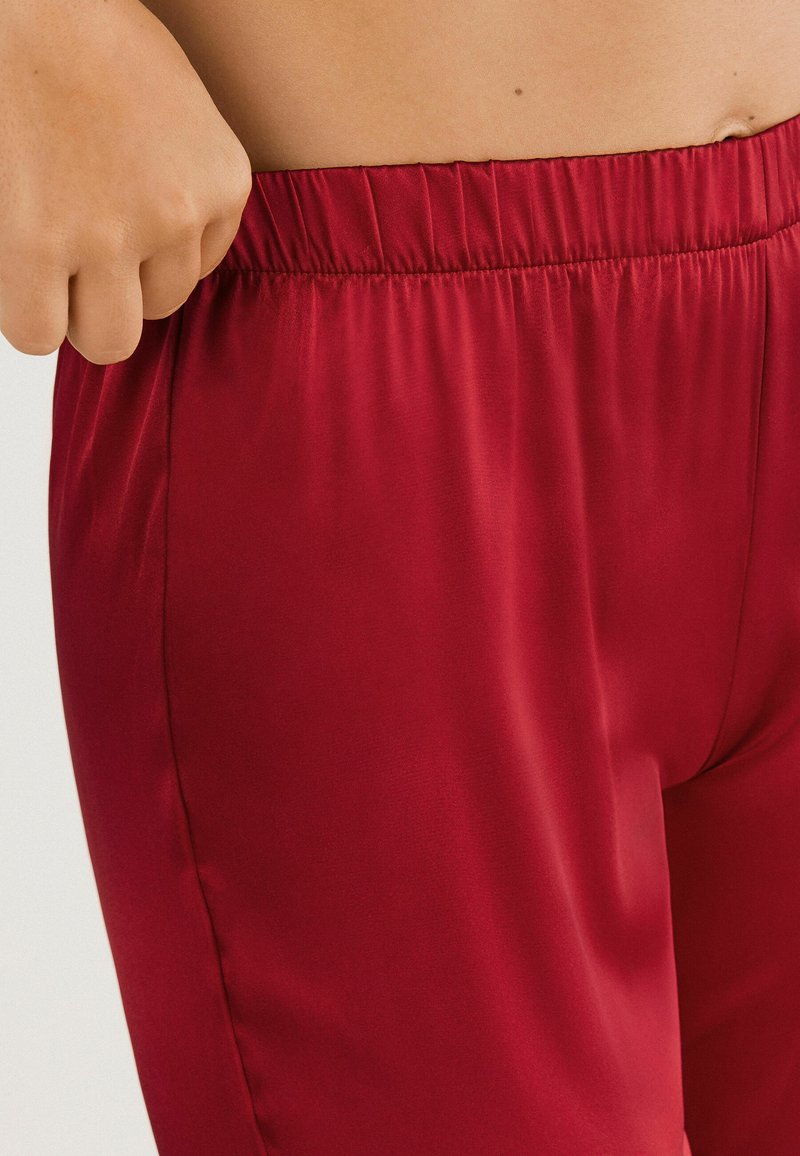 Rode joggers van satijnachtige stof met een elastische tailleband, met een gladde textuur en een aangesloten silhouet. Geen zichtbare patronen of hardware.