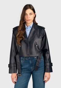 Giacca in ecopelle blu navy tagliata, con chiusura a doppi bottoni, spalle strutturate e dettagli con fibbia sulle maniche. Abbinata a jeans.