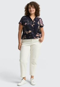 Navy-blaues Blusenshirt mit floralem Muster, kombiniert mit cremefarbenen Hosen und weißen Sneakers. Glattes Material, lockere Passform und Knopfverschluss.