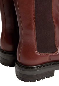 Bottes en cuir marron avec des panneaux élastiques, une surface texturée et des semelles en caoutchouc à profondes rainures pour une meilleure adhérence. Coutures visibles.