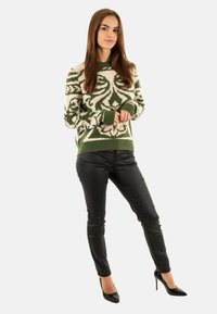 Maglione lavorato a maglia verde e crema con motivi, a maniche lunghe, abbinato a pantaloni neri slim-fit e tacchi alti neri. Sfondo bianco semplice.