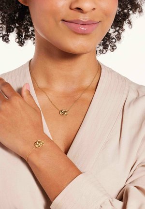 Collier et bracelet en or présentant des motifs circulaires entrelacés. Les chaînes sont délicates, avec une texture lisse contre un haut léger et texturé.
