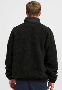 Black fleece pullover with a textured surface. Features a high collar and loose fit. Cuffs and hem are fitted for added warmth.