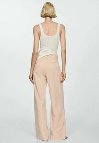 Canottiera bianca e pantaloni a gamba larga rosa chiaro. Il tessuto è leggero, con una texture liscia e un design minimalista. Vista posteriore.