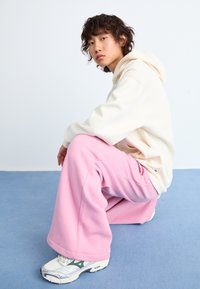 White hoodie paired with baggy pink sweatpants. The outfit features a soft texture, relaxed fit, and casual design. Sneakers complete the look.