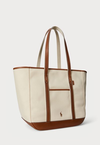 Canvas tote bag i kremfarge med brune lærdetaljer, har to håndtak, en romslig design, og en liten utvendig lomme.