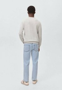 Hellgrauer Pullover mit langen Ärmeln, kombiniert mit hellblauen Jeans mit geradem Bein und beigen Sneakers, von hinten betrachtet.