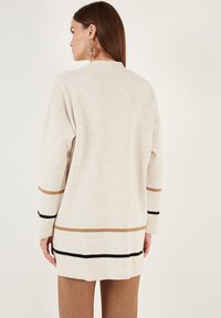 Beige long-sleeve sweater with horizontal stripes in brown and black, featuring a high neckline and relaxed fit, made from knitted material.