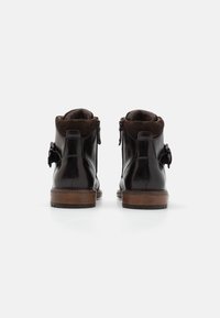 Botas de cuero marrón hasta el tobillo con un acabado suave, cierre de cremallera y un cuello de ante marrón oscuro. Tacón de madera y acento decorativo de lazo.