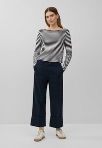 Camicia a righe con maniche lunghe in bianco e nero, abbinata a pantaloni larghi blu navy con orlo a risvolto, indossati con sneakers bianche e beige.