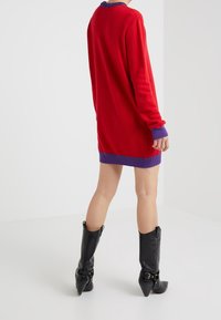 Red knitted sweater dress with purple cuffs, featuring a crew neck and long sleeves, paired with black knee-high heeled boots.