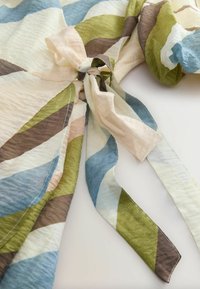 Tissu aux rayures diagonales bleu, vert, marron et crème, noué en un nœud lâche sur une surface claire.