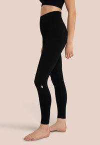 Leggings neri a costine con fascia alta in vita, caratterizzati da un logo sulla gamba inferiore. Il tessuto sembra morbido e aderente.