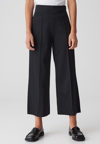 Pantalons noirs taille haute avec jambes larges, comportant des plis avant, une texture lisse et un design de taille épuré. Style classique et polyvalent.