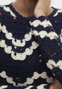 Maglione all'uncinetto blu navy e crema con motivi a onda, bordi scallop e una finitura texturizzata. Maniche lunghe con dettagli a giorno.