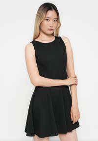 Robe noire sans manches avec un corsage ajusté et une jupe évasée, fabriquée en tissu lisse. Dotée d'un col rond et de coutures décoratives.