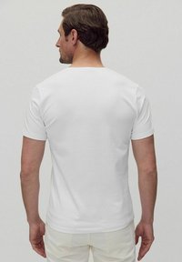 Vit T-shirt med korta ärmar och rund halsringning, visad bakifrån på en neutral bakgrund.