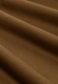 Tissu en coton brun à texture lisse, présentant de légers plis et une couleur uniforme sans motifs ni accents.