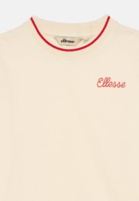 Kremfarget T-skjorte med rød ribbestrikket hals og en rød brodert "Ellesse"-logo på fronten. Mykt bomullsmateriale, kort erm.