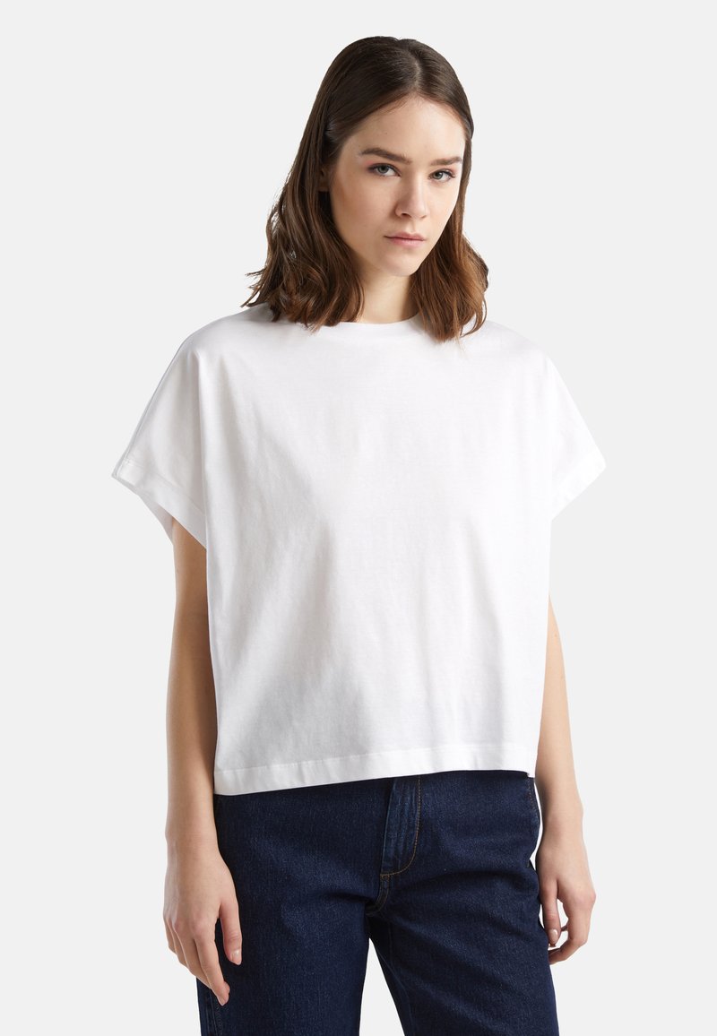 T-shirt bianco a maniche corte in cotone con una vestibilità morbida, scollo rotondo e un orlo che cade alla vita, abbinato a jeans blu scuro.