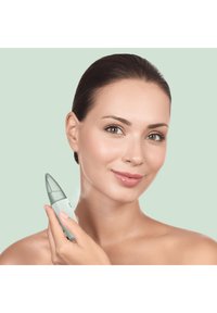 Appareil de beauté portable avec un corps vert menthe lisse et une buse transparente. L'utilisateur le tient contre sa joue, mettant en avant un design élégant et ergonomique.