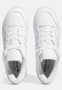 Vita sportskor i läder med en slät textur, med perforeringar, snörning och tre sidostriper. Tydlig branding på tungan.