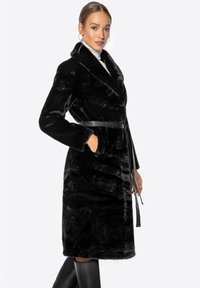 Černý kabát z umělé kožešiny s šálovým límcem, dlouhými rukávy a umištěným páskem v pase. Obsahuje boční kapsy a hladkou texturu. Délka ke kolenům.