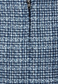 Gros plan sur un tissu tissé bleu et blanc avec une fermeture éclair argentée partiellement zippée, courant verticalement à travers le centre.