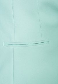 Lysblåt stof med en subtil tekstur, der har en vandret slidslomme i en skræddersyet design. Fokuserer på rene linjer og minimalistisk stil.
