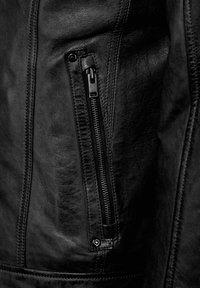 Details van een zwart leren jack met een ritszak, een gestructureerd oppervlak en zichtbare stiksels naast hardware-accenten.