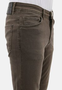 Donkerbruine denim jeans met een slim fit, voorzien van voorzakken, subtiele stiksel en een leren label op de tailleband.