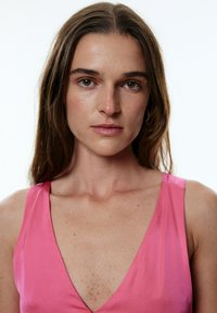 Rosa Satin-Kleid mit tiefem V-Ausschnitt und breiten Trägern, das eine glatte Textur schafft und subtile Farbvariationen sowie eine figurbetonte Silhouette aufweist.