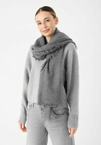Grijze wollen sjaal in een blend met franjes, nonchalant om de nek gewikkeld. Zachte textuur die past bij een lichtgrijze trui en broek.