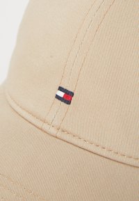 Beige bomuldske med en ribbet tekstur. Har et lille broderet logo i rød, hvid og marineblå farver på siden.