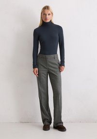 Donkerblauwe coltrui gecombineerd met hoog opgesneden, grijs geblokte broek en bruine suède schoenen. Glad materiaal, getailleerde pasvorm en subtiele patronen.