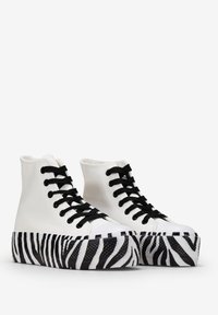 Hoch geschnürte Sneakers mit einem weißen Canvas-Obermaterial, schwarzen Schnürsenkeln und einer Plattformsohle im gestreiften Zebra-Design. Strukturierte Schwarz- und Weißakzente.
