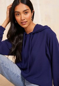 Felpa blu navy con una vestibilità comoda, polsini a coste, cappuccio con cordino e texture morbida, abbinata a jeans azzurri.