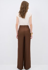 Bruine wijde broek met een hoge taille en riemlussen, gemaakt van textuurstof; gecombineerd met een beige top met korte mouwen.
