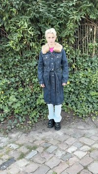 Casaco trench de ganga com gola de pelúcia sintética, cintura com cinto, mangas longas, cor azul, combinado com calças claras e sapatos pretos robustos.