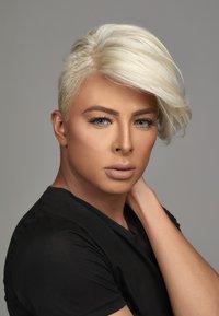 Il ritratto presenta una persona con i capelli corti, biondo platino, acconciati su un lato, che indossa una camicia nera aderente e un trucco neutro.