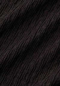 Tissu noir avec des lignes verticales denses, irrégulières et en relief créant un motif texturé et ondulé.