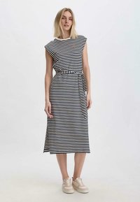 Gestreiftes Kleid aus Marineblau und Creme mit kurzen Ärmeln, einem taillierten Bund mit einem Bindeband und einem geraden Saum. Kombiniert mit hellen Sneakers.