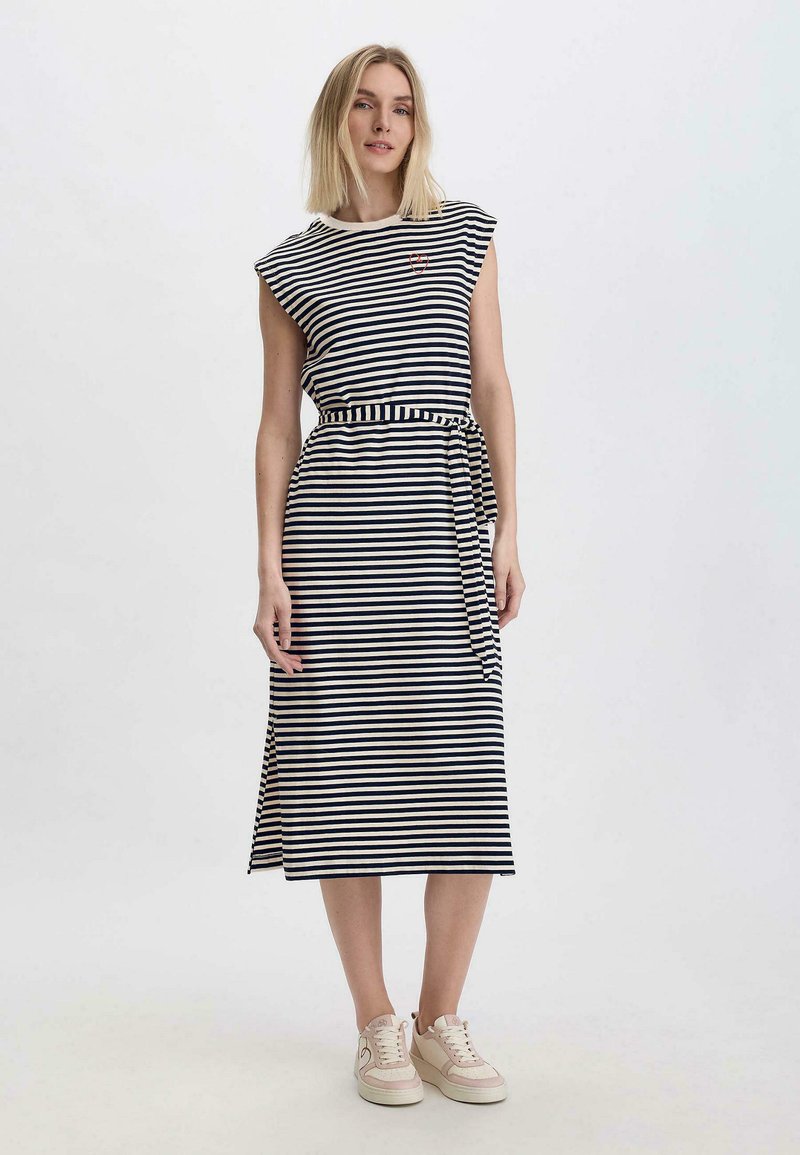 Gestreiftes Kleid aus Marineblau und Creme mit kurzen Ärmeln, einem taillierten Bund mit einem Bindeband und einem geraden Saum. Kombiniert mit hellen Sneakers.