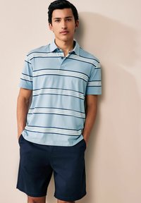 Polo de color azul claro con patrones rayados en tonos oscuros y claros, de mangas cortas y con collar; combinado con pantalones cortos azul marino oscuro. Textura suave.