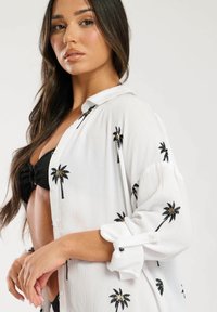 Camisa blanca de botones con bordado de palmeras negras, con una textura ligera, mangas enrollables y un corte relajado.
